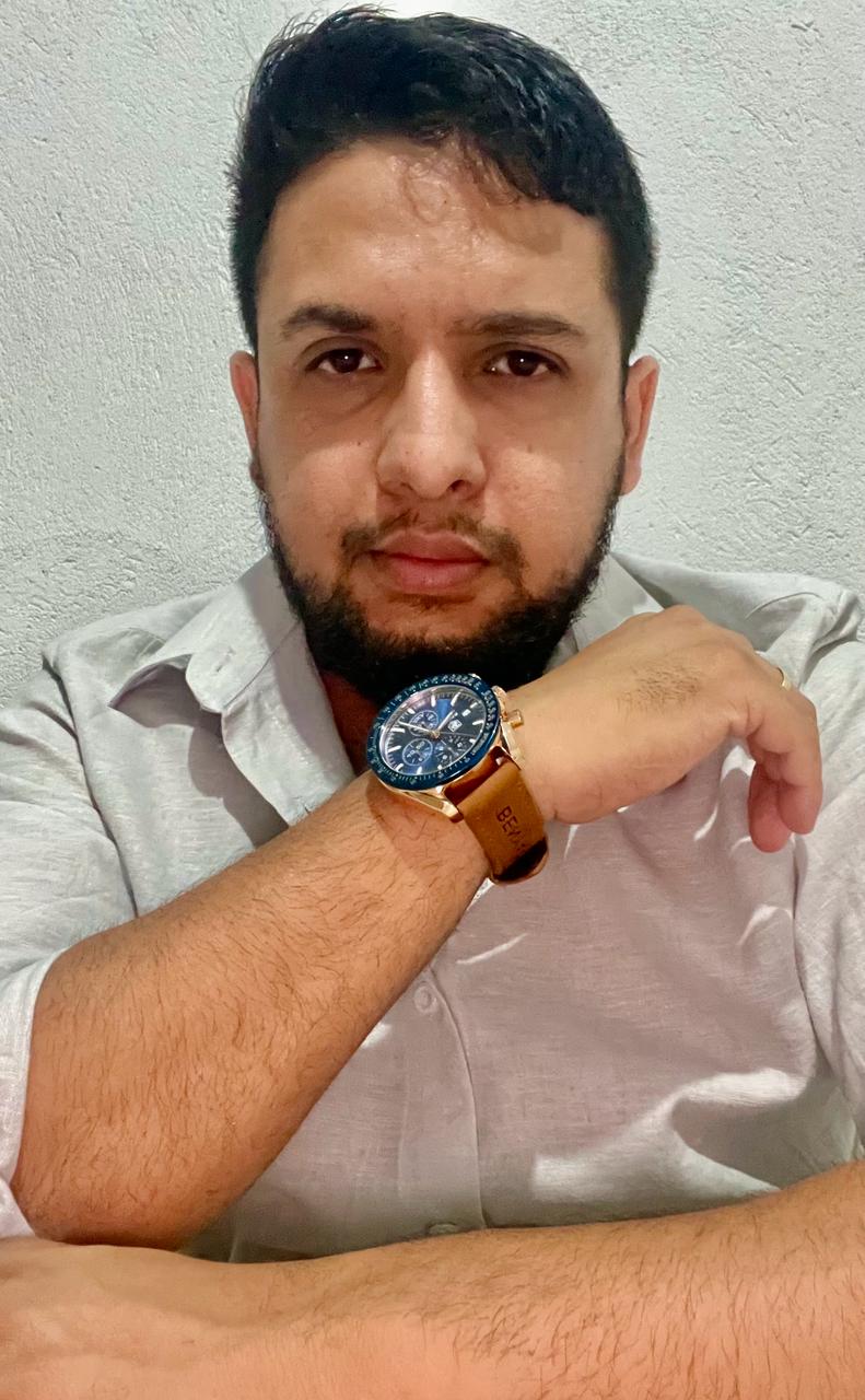 Imagem de Ruan torres vestindo camisa social branca e sorrindo com plantas no fundo